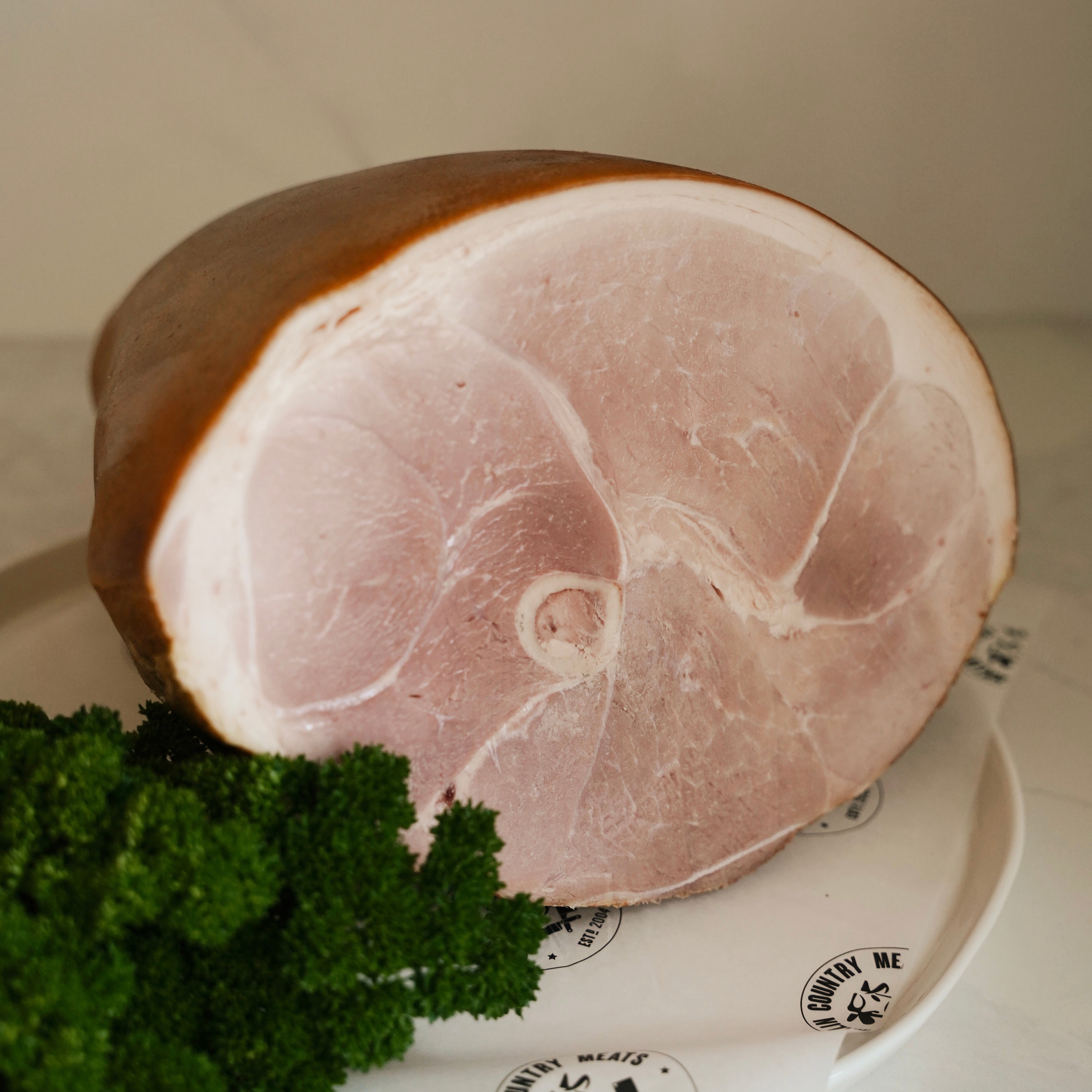 Raw ham on a white plate with green herbs.